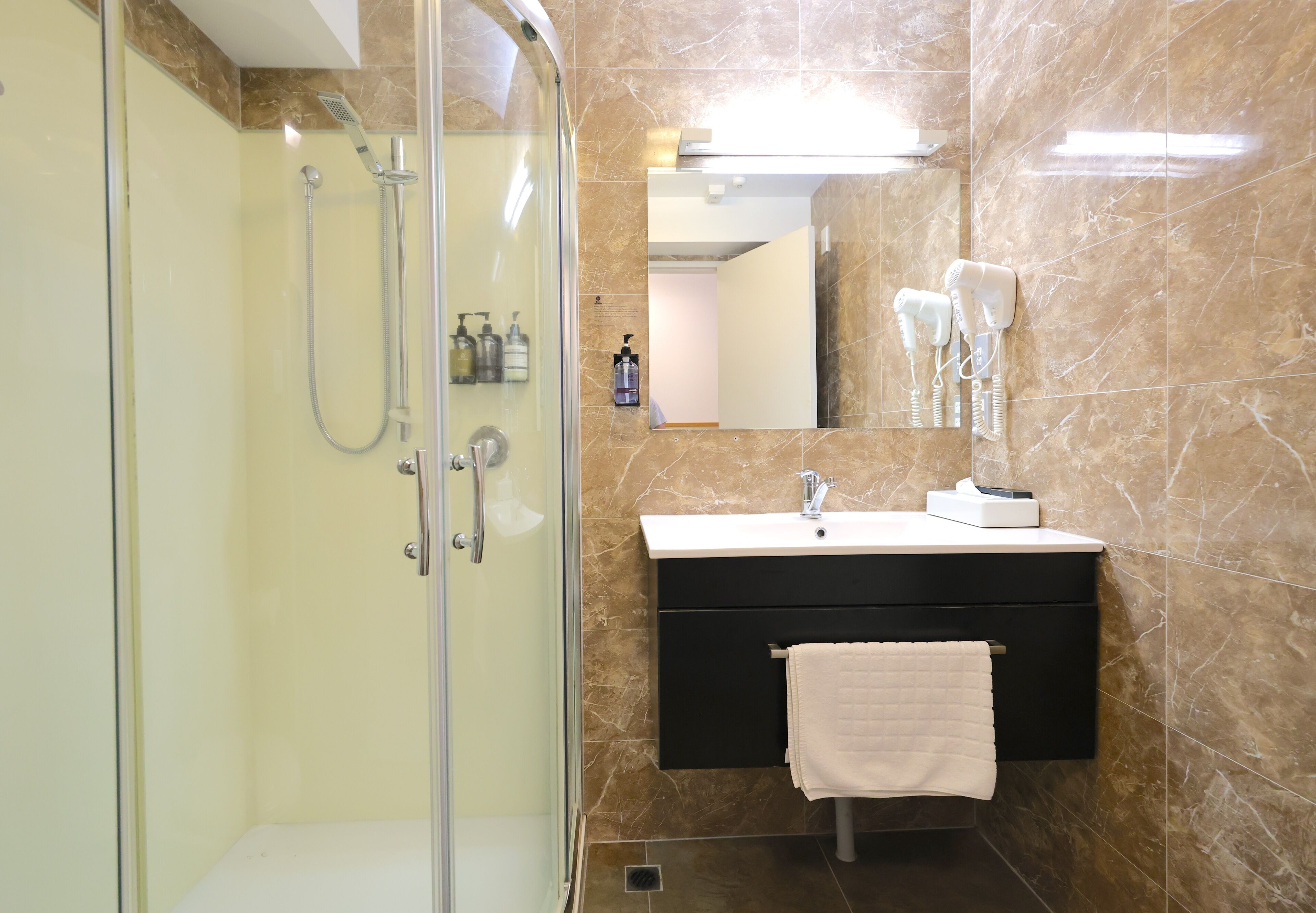 A modern bathroom with a glass-enclosed shower, a black vanity with a white sink, and a towel hanging on the wall.