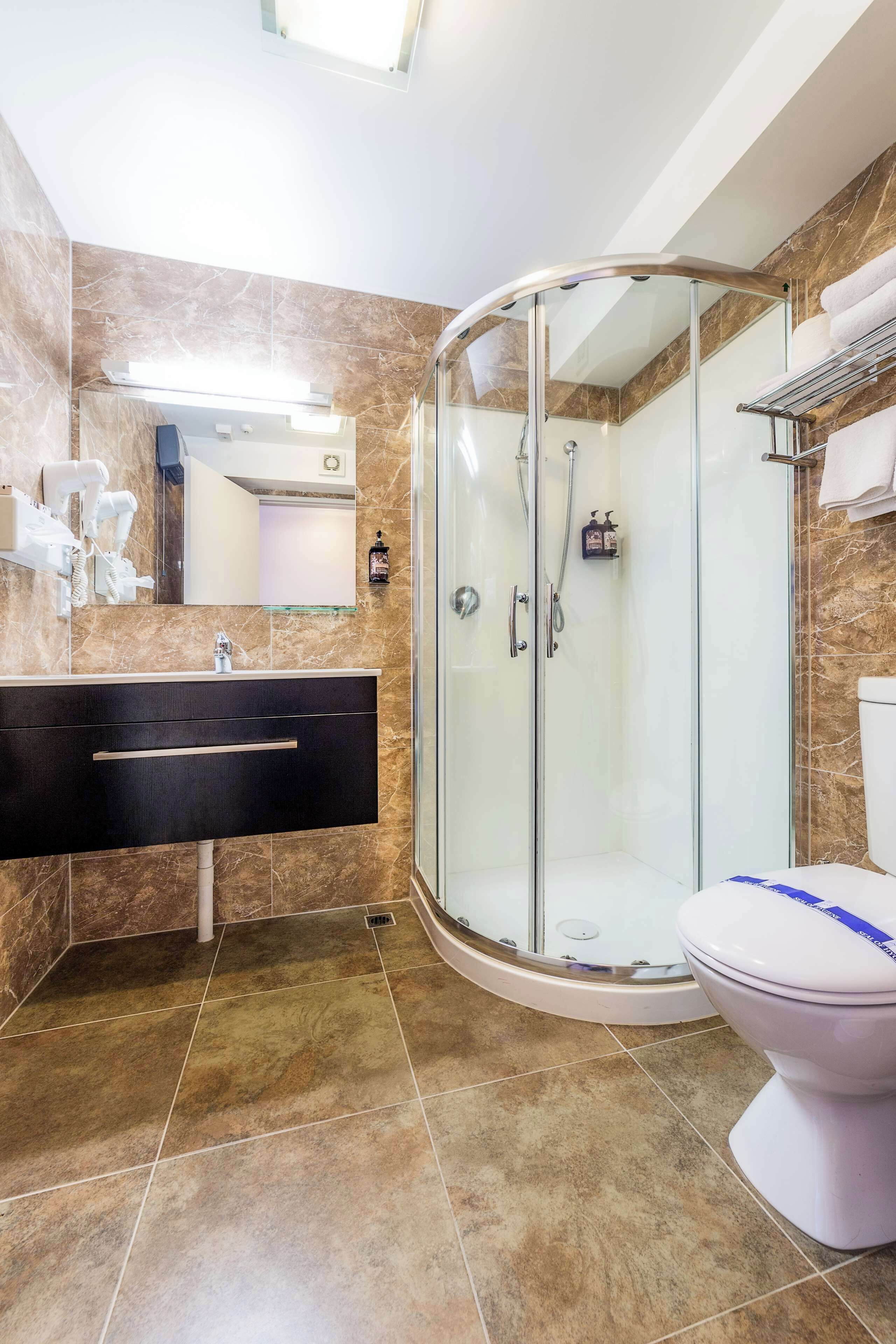 A modern bathroom with a curved glass shower enclosure, a white toilet, and a black vanity with a mirror.