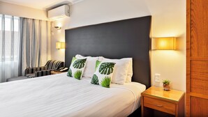 Una camera d'albergo con un letto grande, un comodino con una lampada, una sedia e una finestra con tende.