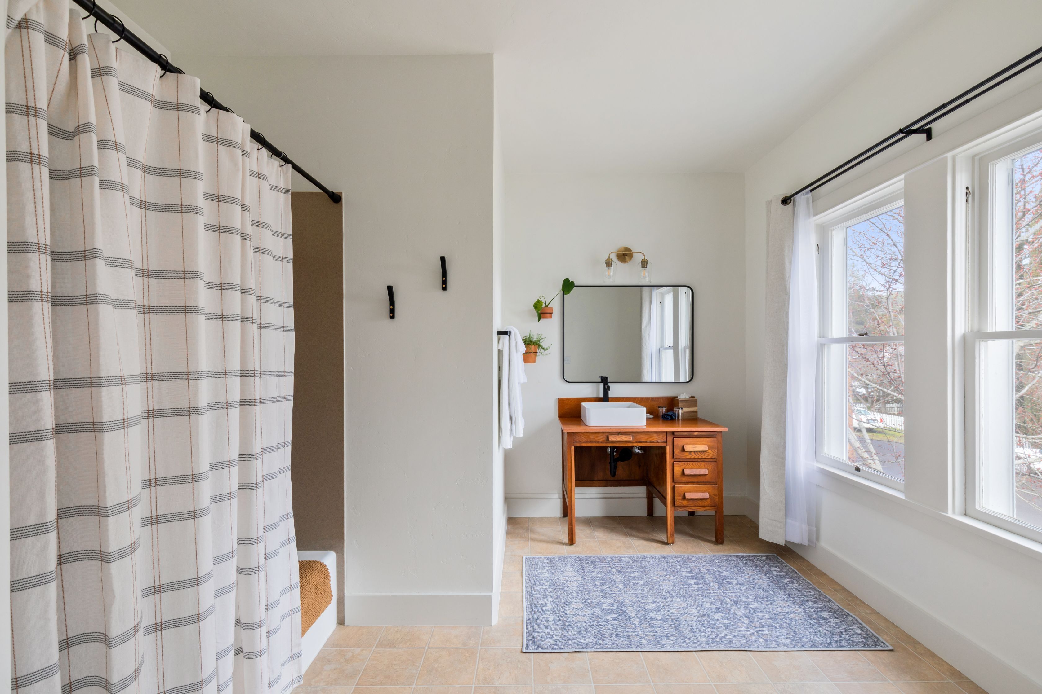 A bathroom with a wooden vanity, a mirror, a window, and a shower curtain.