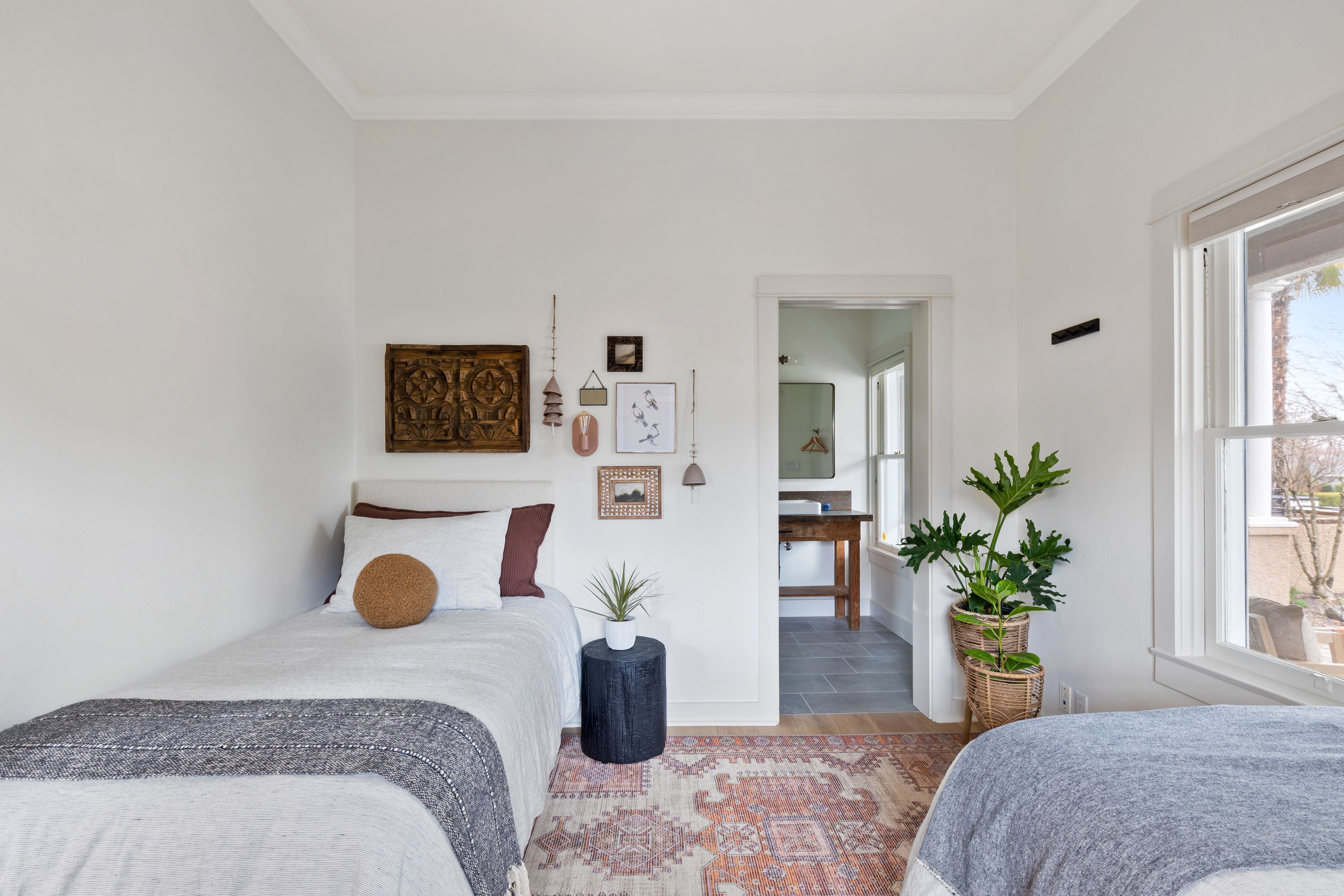 A bedroom with two beds, a large window, and a view of a dining area.