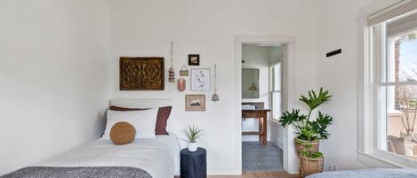 A bedroom with two beds, a large window, and a view of a dining area.