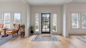 A spacious entryway with a dark wooden door, large windows, a rug, a chair, and a small table with a plant. - Magnolia Hotel (Jacksonville)