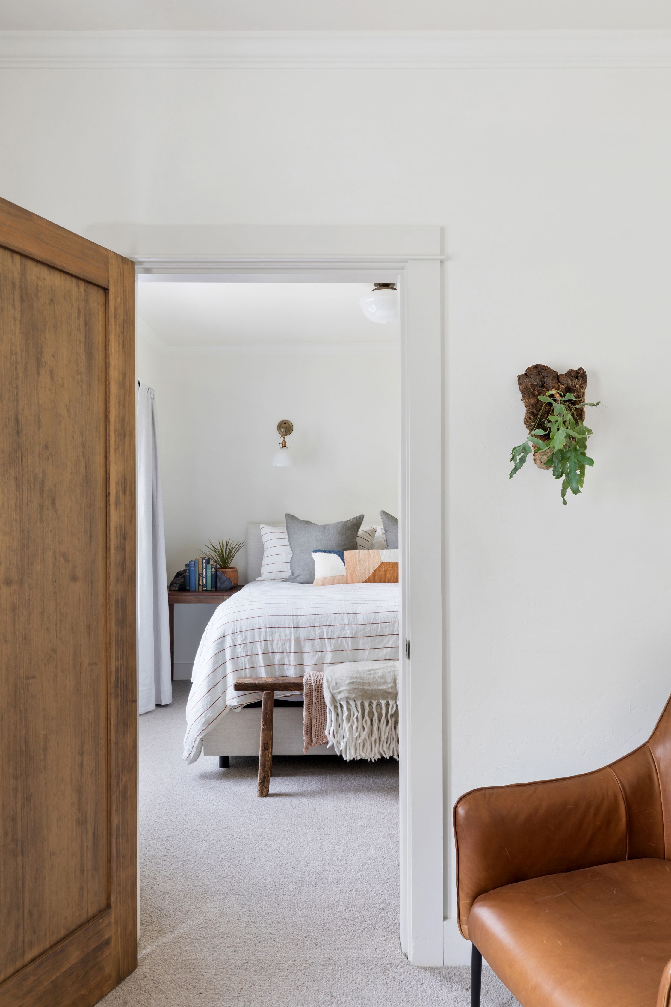 A bedroom with a bed, bedside table, and a hanging plant.