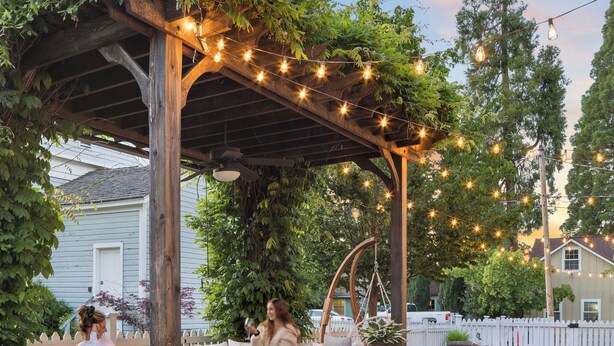 An outdoor patio with seating under a pergola, string lights, and a fire pit. - Magnolia Hotel (Jacksonville)