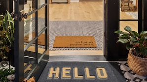 A hotel entrance with a black door, a '245' sign above, and a 'HELLO' mat at the threshold. - Magnolia Hotel (Jacksonville)