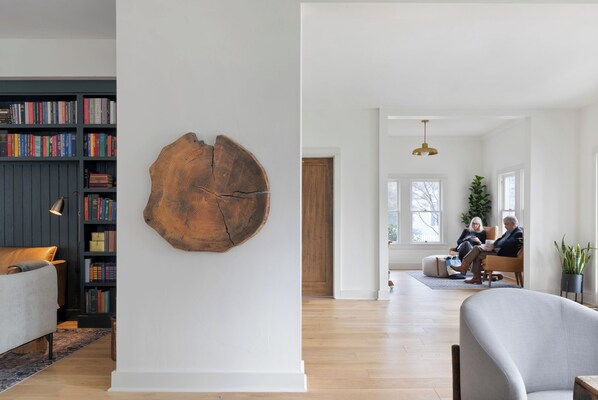 Un salon moderne avec une bibliothèque, une grande œuvre d’art murale en bois et un couple assis sur un canapé.