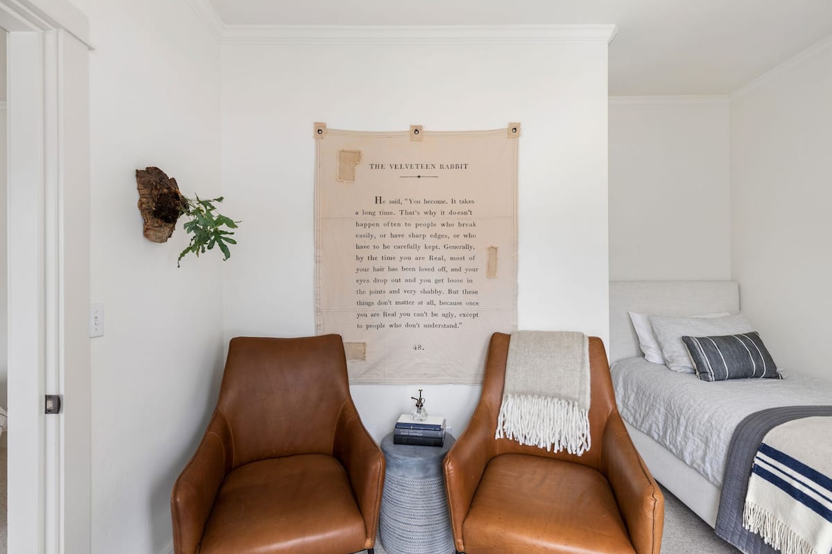 Une chambre à coucher avec un lit, deux fauteuils en cuir, une plante fixée au mur et une affiche.