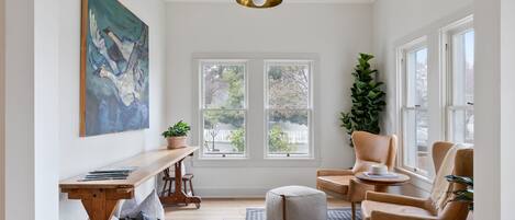 Una habitación luminosa y bien iluminada, con un ventanal grande, una mesa de madera, una silla cómoda y una planta en maceta.