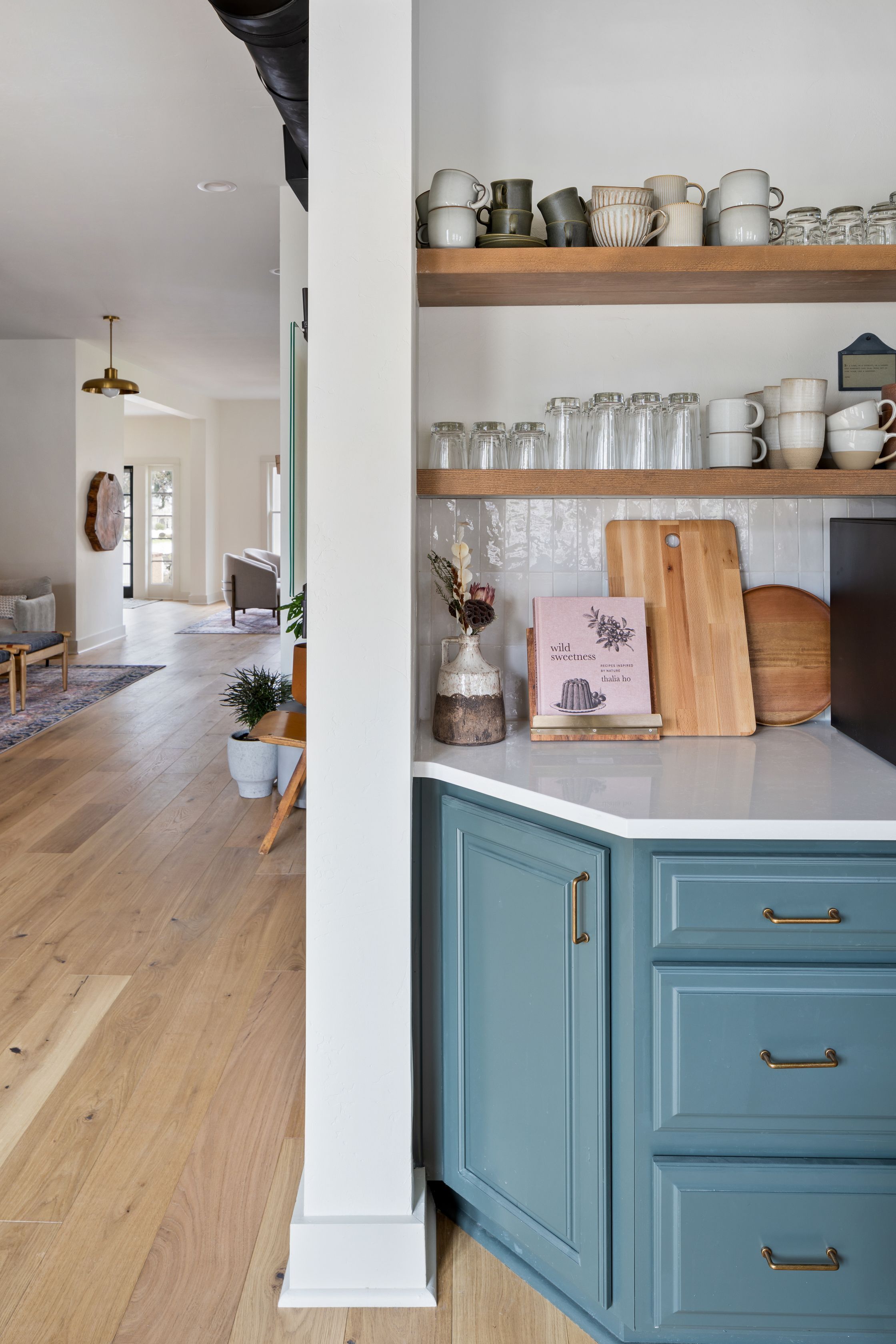 A kitchen with wooden shelves holding various kitchenware, a cutting board, and a book titled "wild sweetness."