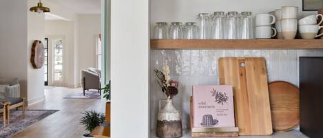 A kitchen with wooden shelves holding various kitchenware, a cutting board, and a book titled "wild sweetness."
