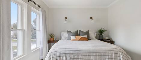 Een slaapkamer met een groot bed, twee nachtkastjes, een raam met gordijnen en een plafondlamp.