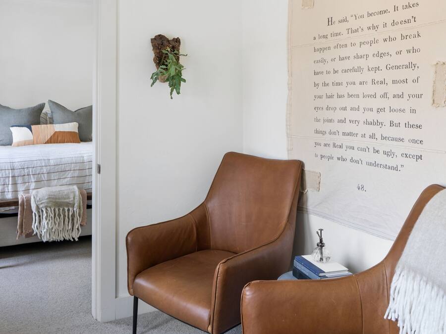 A bedroom with a large bed, a brown leather chair, and a wall-mounted book titled "The Velvet Teen Rabbit".