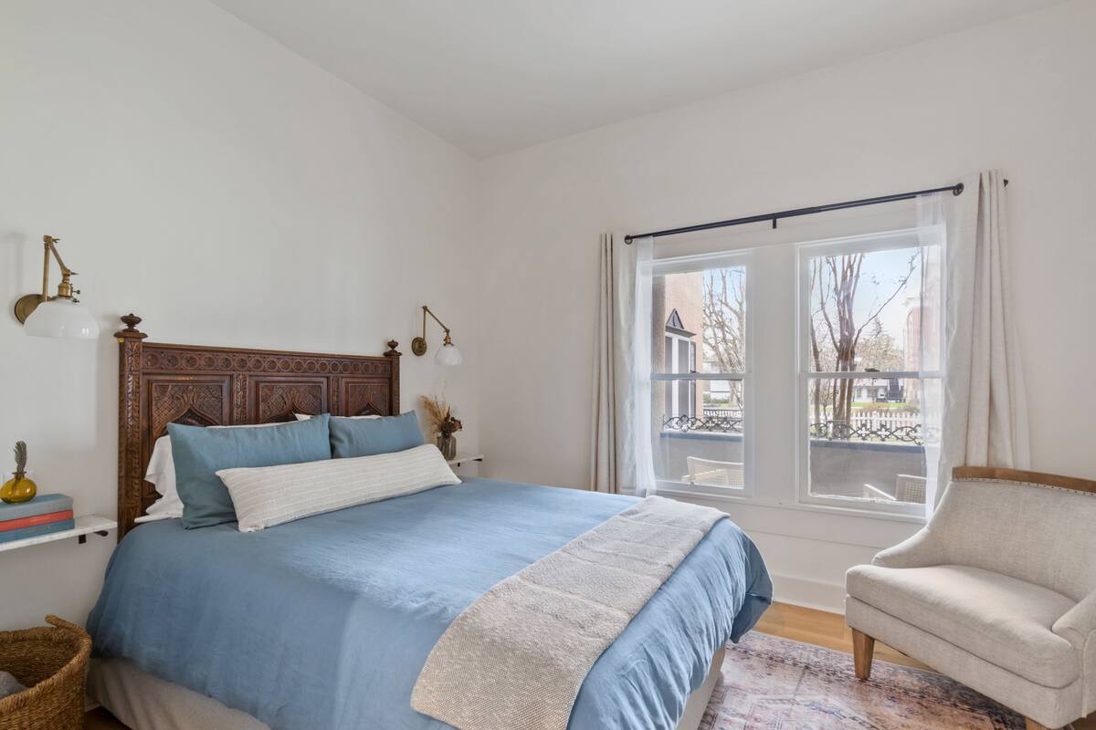 Une chambre à coucher avec un grand lit, une chaise, une fenêtre avec des rideaux et une vue sur l’extérieur.