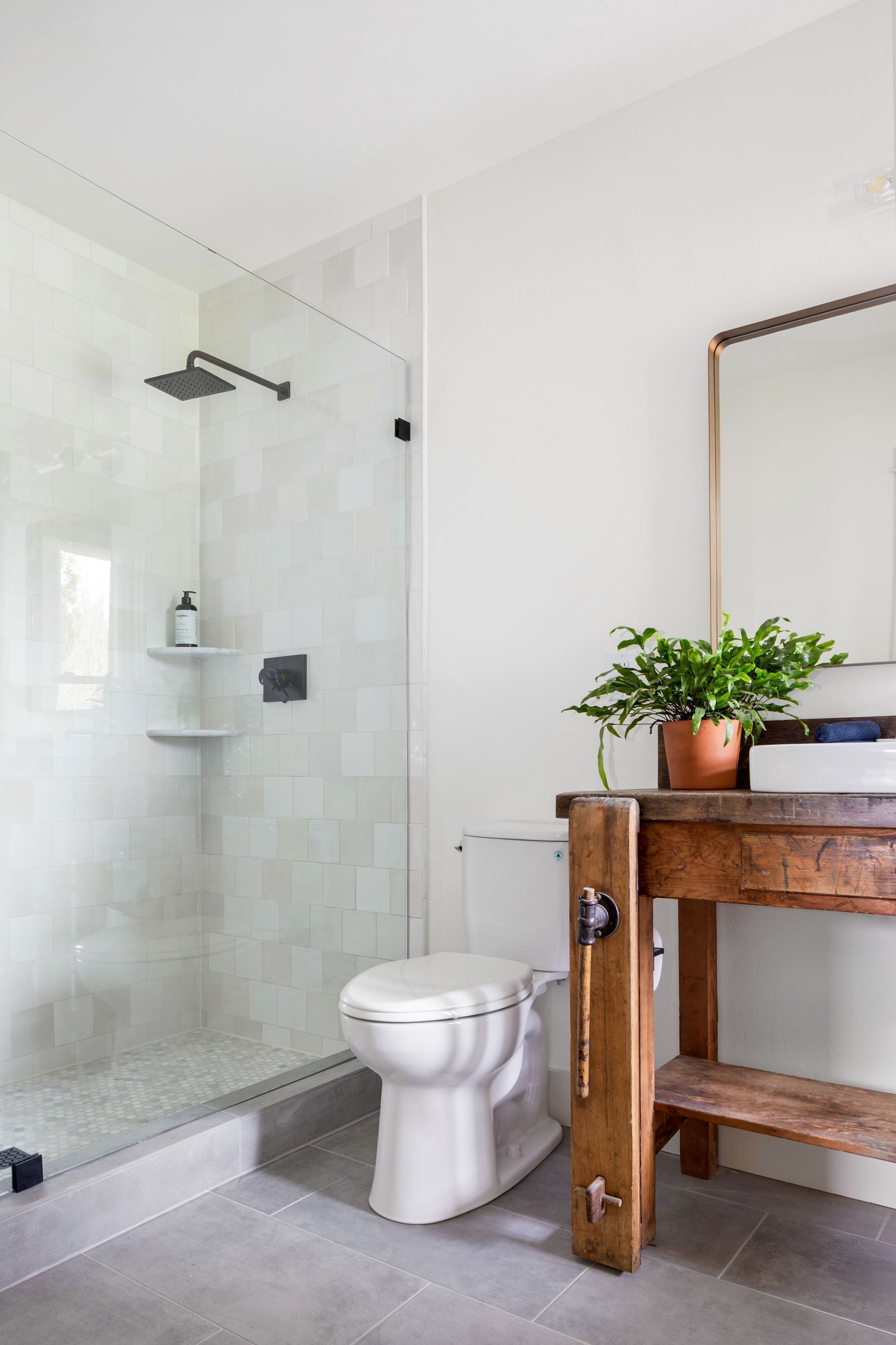 Une salle de bain avec une douche à parois de verre, des toilettes blanches et un meuble-lavabo en bois avec un miroir.