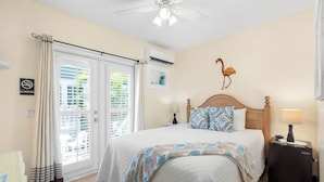 A bedroom with a bed, nightstand, lamp, air conditioning unit, and a no smoking sign. - The Grand Guesthouse (Key West)