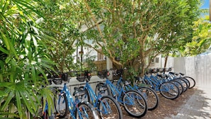 A row of blue bicycles parked under a tree, with a white fence and a building in the background. - The Grand Guesthouse (Key West)