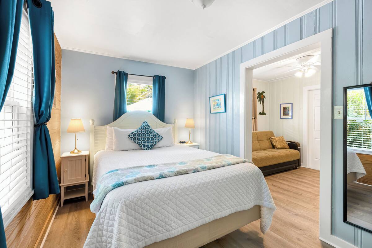 A bedroom with a large bed, two bedside tables with lamps, a sofa, and a mirror.