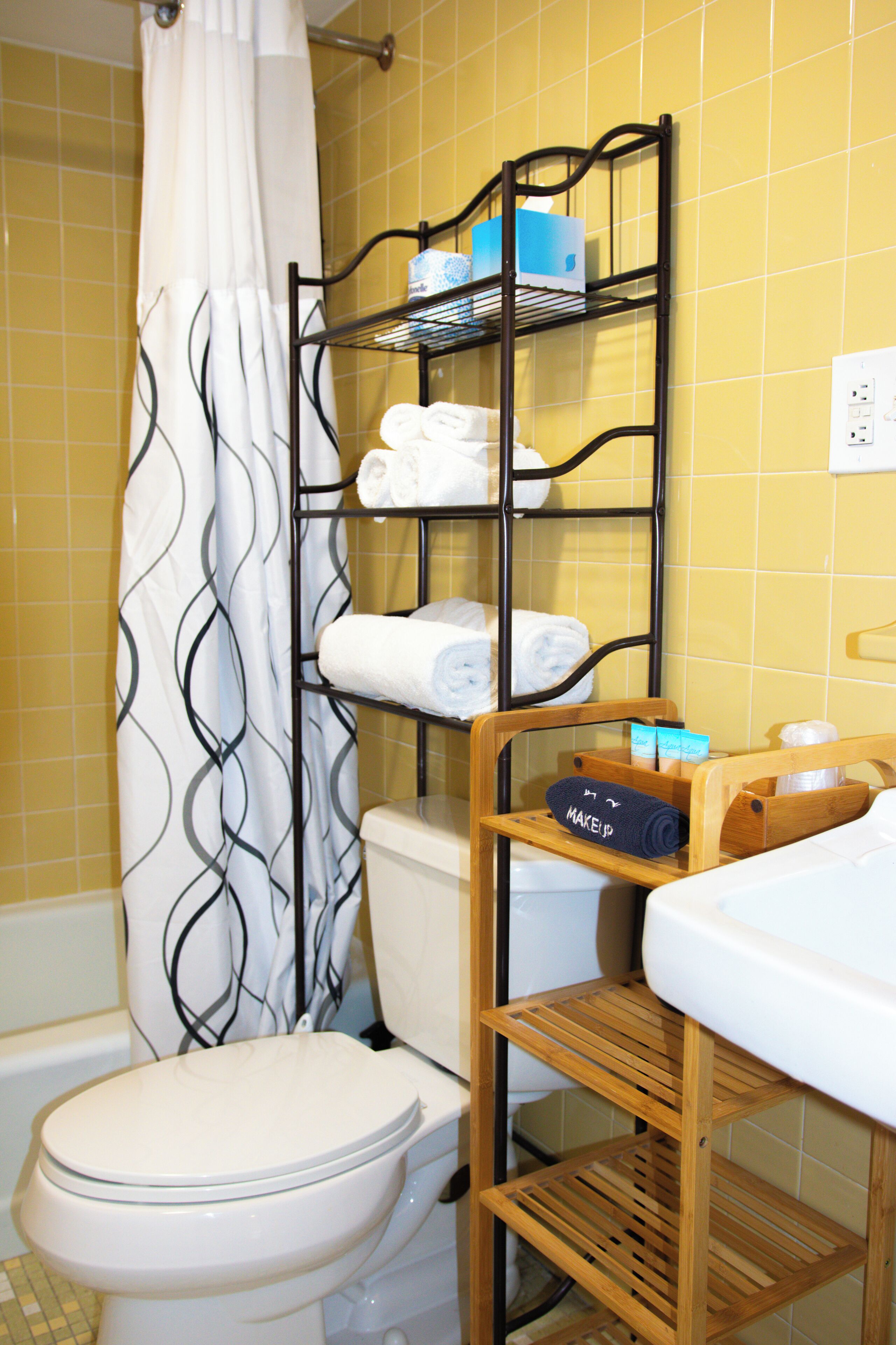 Une salle de bain comprenant des toilettes, un rideau de douche, une étagère avec des serviettes et un porte-savon en bois pour les articles de toilette.