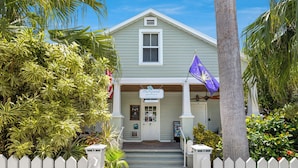 A two-story building with a porch, a sign reading "The Grand Guesthouse," and a purple flag. - The Grand Guesthouse (Key West)