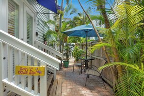 A private patio area with a wooden deck, a table with chairs, and a sign indicating 'Room 2 Private Patio'. - The Grand Guesthouse (Key West)