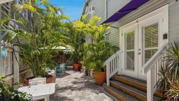 A narrow outdoor pathway flanked by potted plants and a wooden staircase leading to a white door with shutters. - The Grand Guesthouse (Key West)