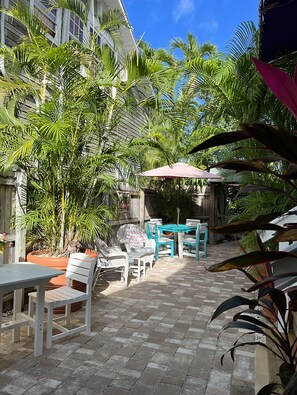 An outdoor patio with a table and chairs, surrounded by potted plants and palm trees. - The Grand Guesthouse (Key West)