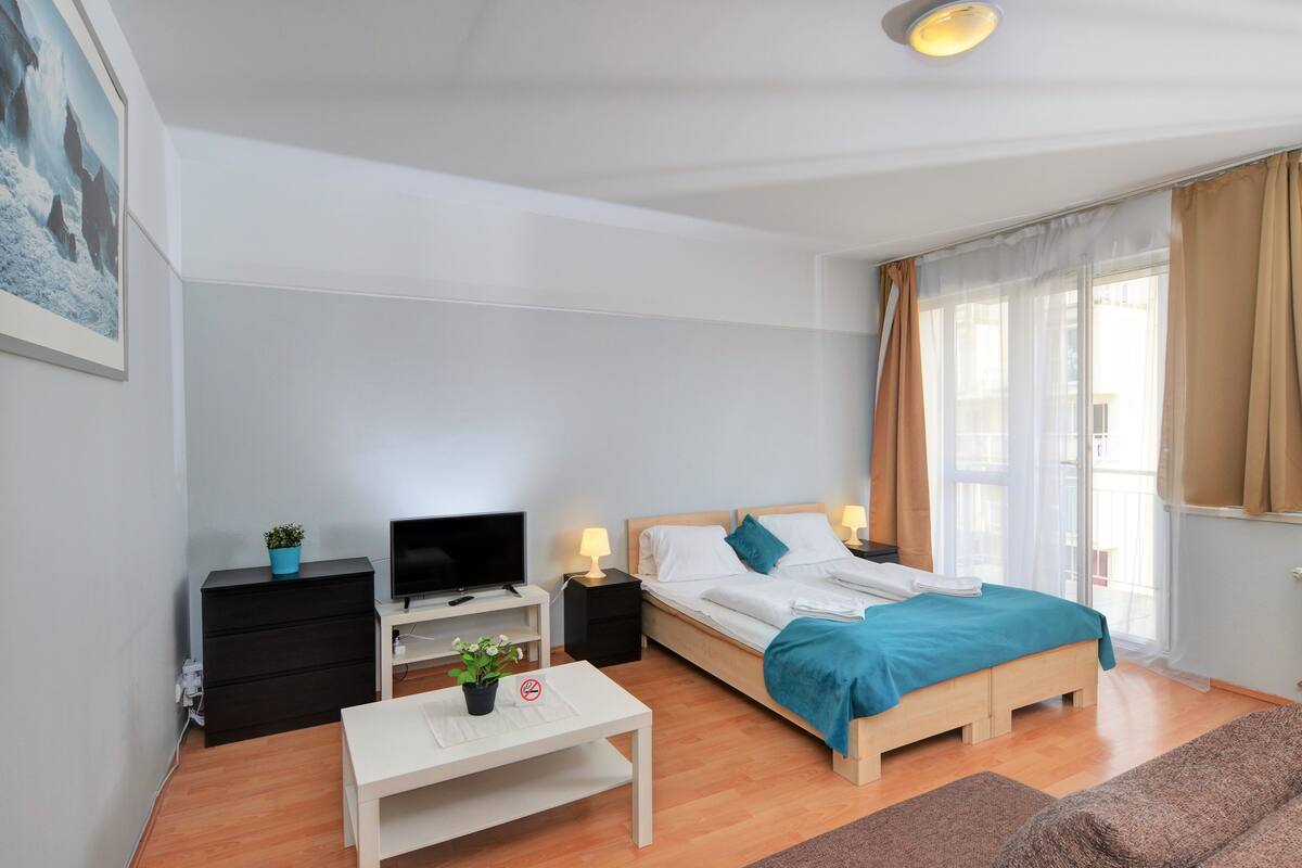 A modern bedroom with a bed, bedside tables, a desk, a TV, and a window with curtains.
