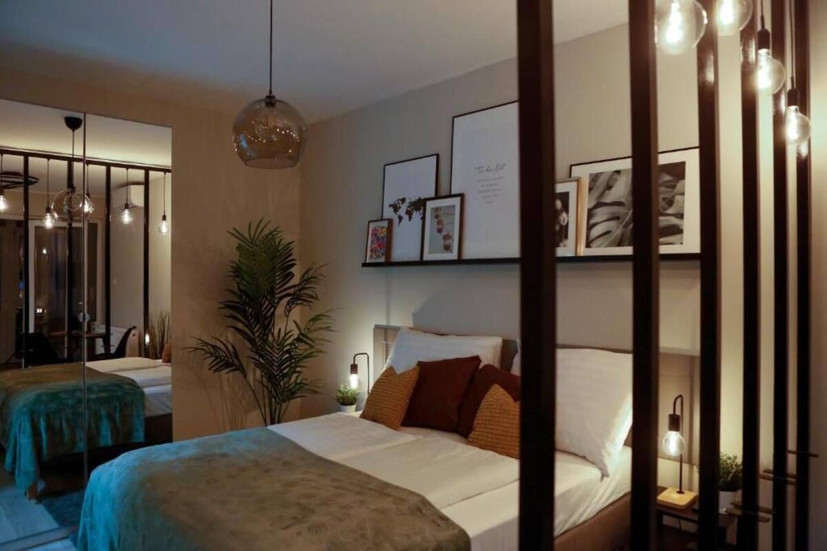 A hotel room with two beds, a large potted plant, framed artwork on the wall, and pendant lighting.
