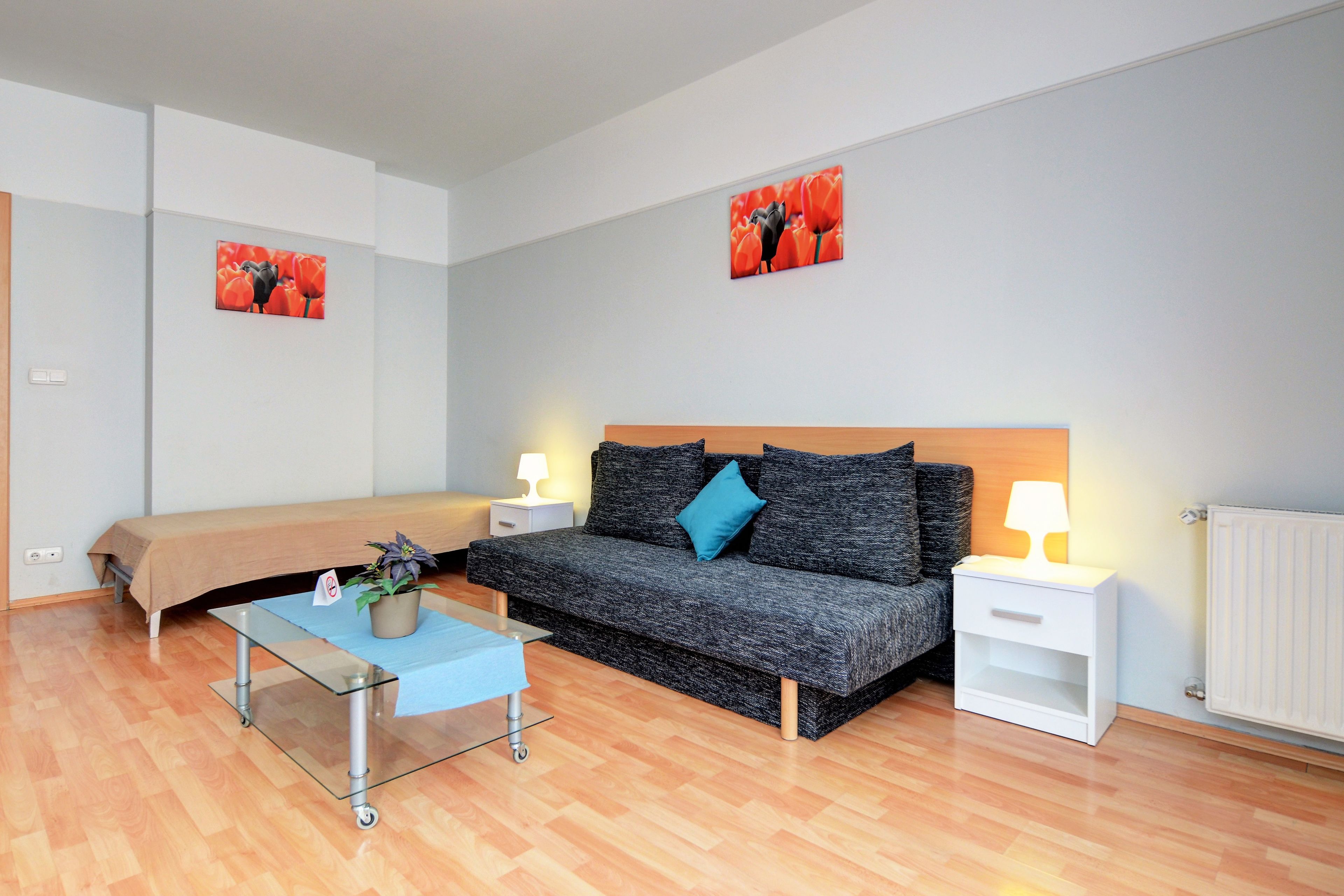 Una habitación moderna y bien iluminada con un sofá, una mesa de centro de vidrio, una mesita de noche con lámpara y dos cuadros colgados en la pared.