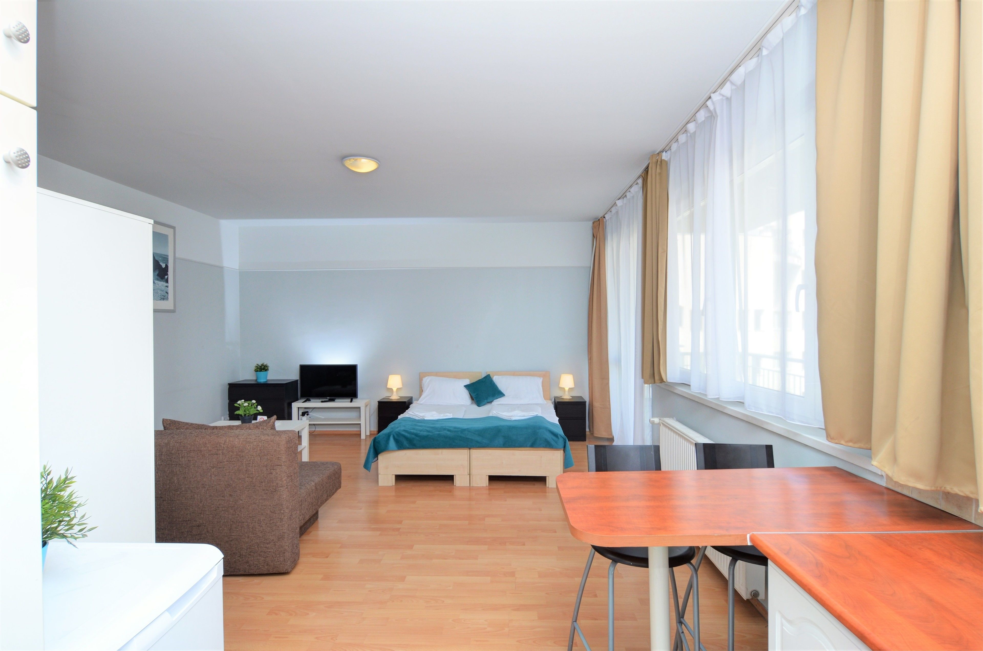A hotel room with a bed, a desk, a chair, a sofa, and a window with curtains.