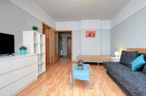 Une pièce moderne et bien éclairée, équipée d’un téléviseur à écran plat, d’un canapé, d’une petite table avec une plante et d’un lit avec une table de chevet.