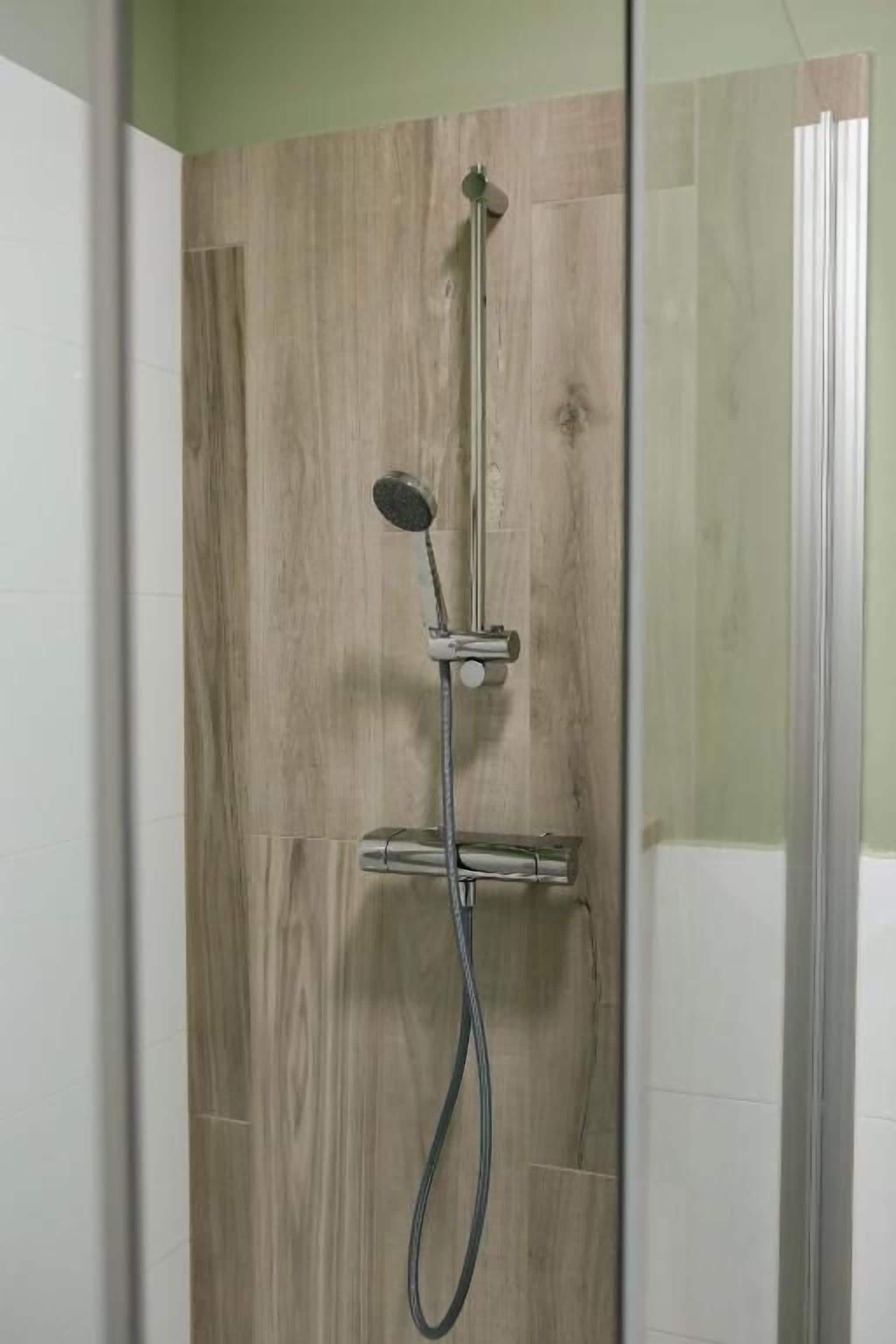 A shower with a handheld showerhead and a wall-mounted control panel.
