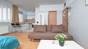 Ein modernes Wohnzimmer mit einer Couch, einem Couchtisch mit Pflanze und Blick auf eine Küche und Essbereich.