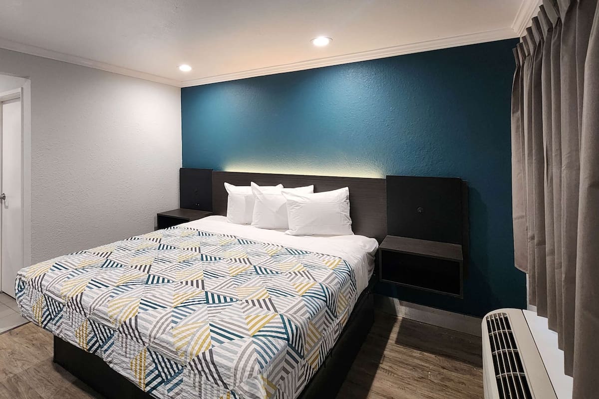 A modern hotel room with a large bed, a bathroom with a mirror and sink, and a blue accent wall.