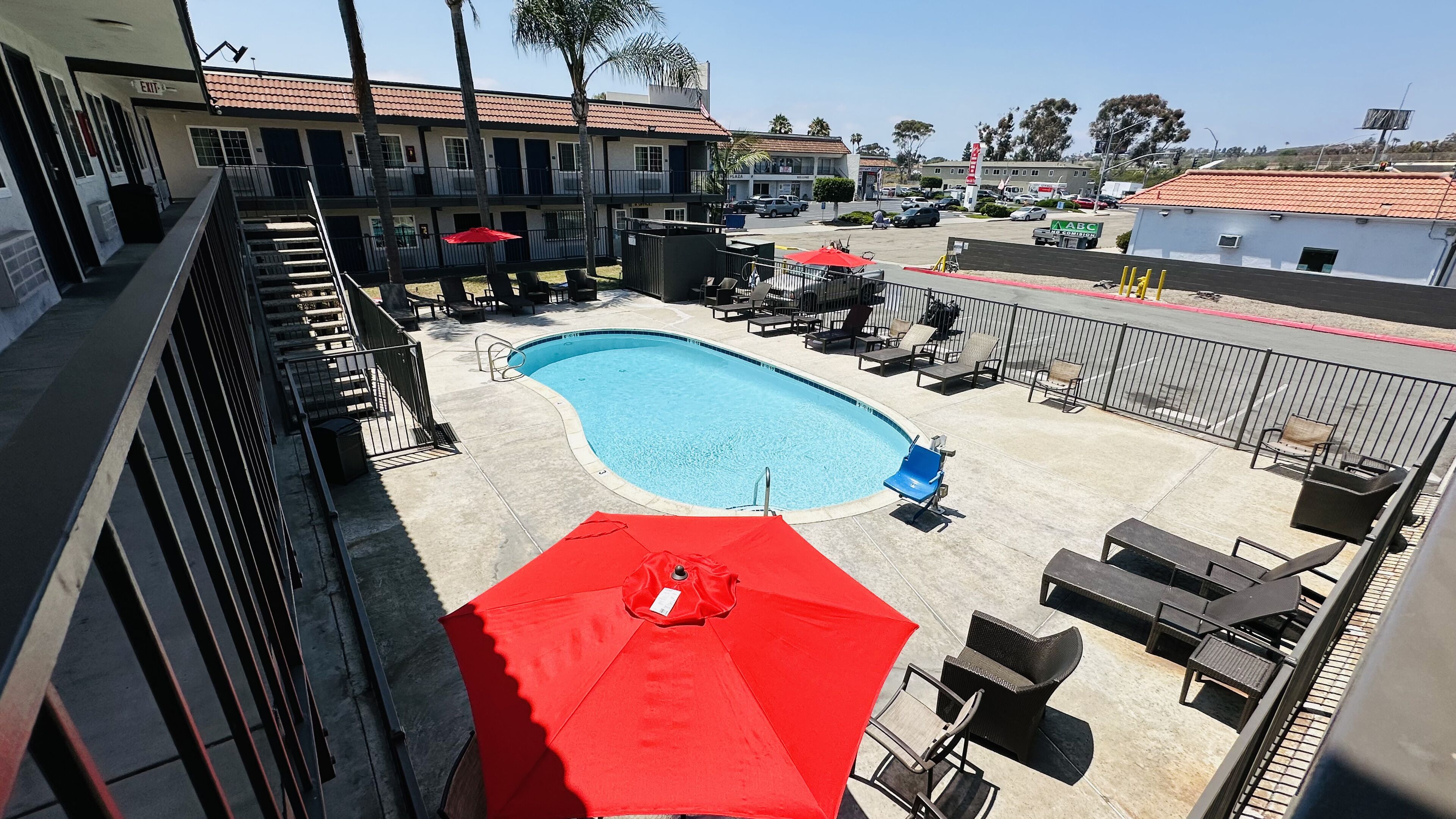 A pool area with a red umbrella, lounge chairs, and a building in the background.