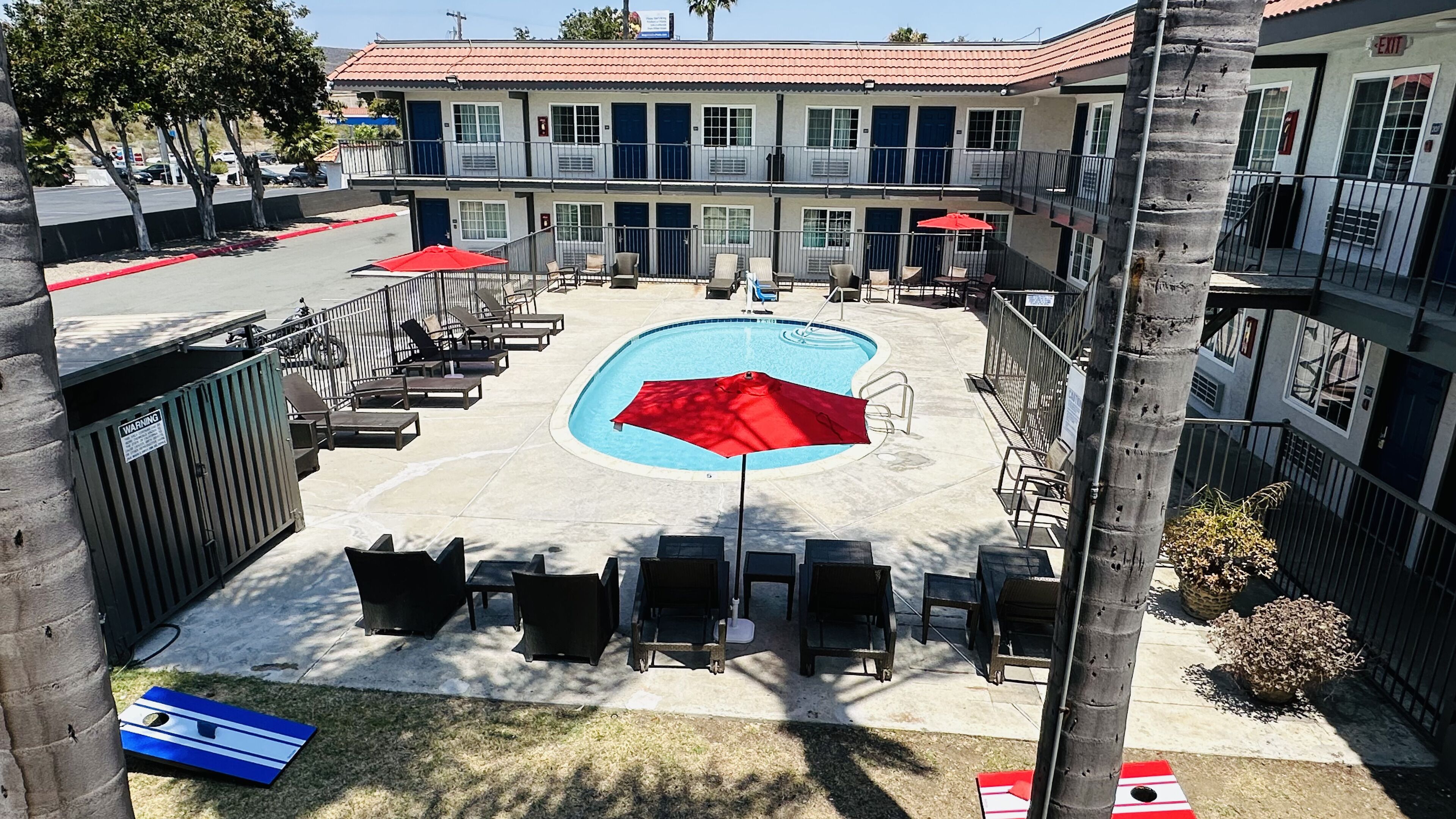 Une cour d’hôtel avec une piscine, des chaises longues et des parasols.