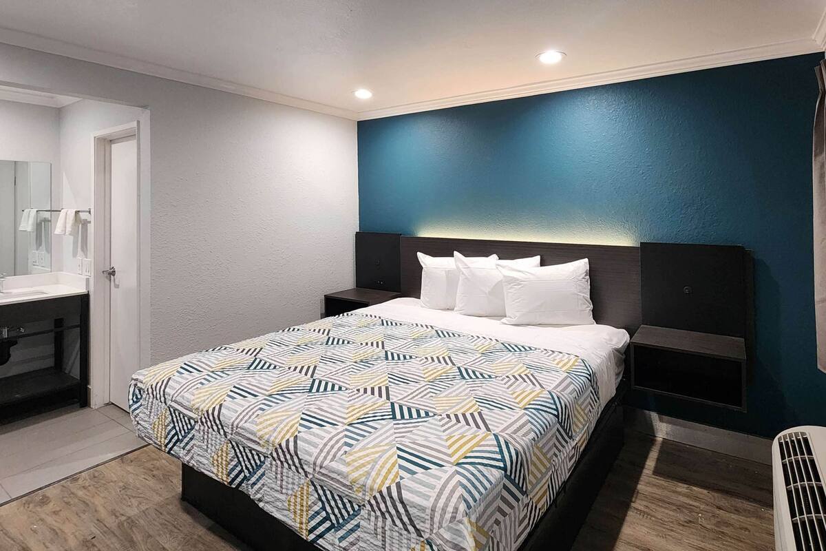 A modern hotel room with a bed, bedside tables, a mirror, and a bathroom.
