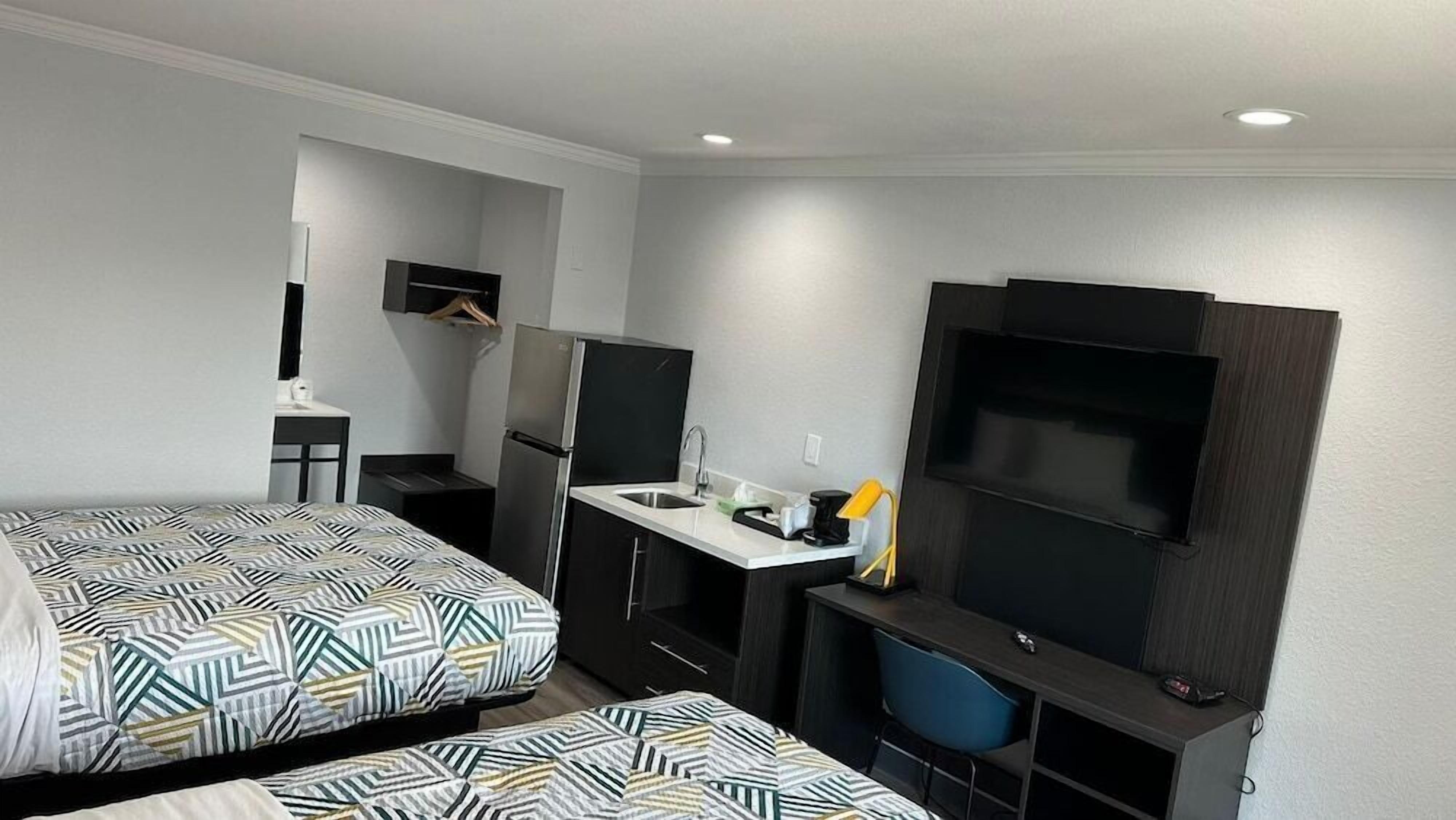 Habitación de hotel compacta con dos camas, kitchenette, televisor y escritorio.