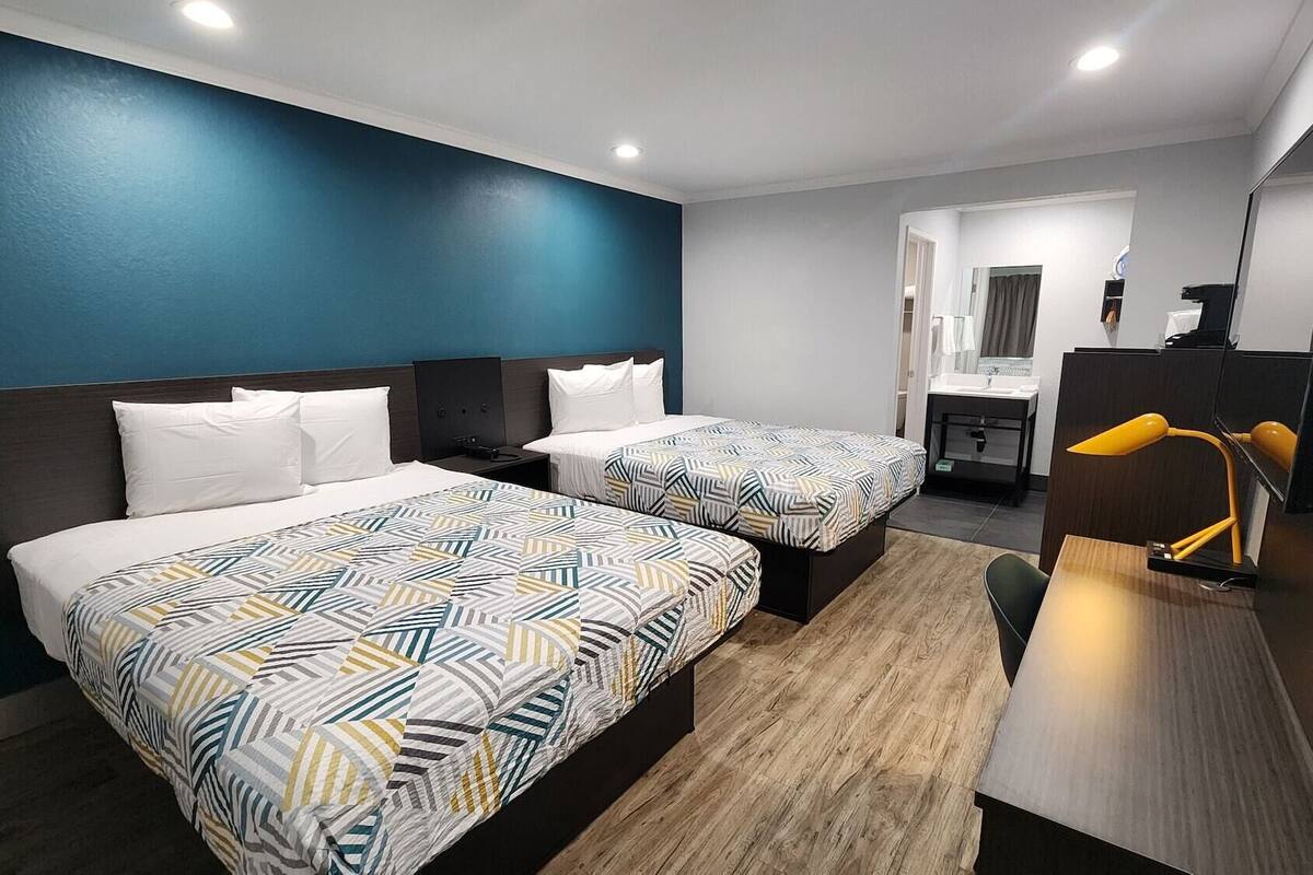A hotel room with two beds, a desk, a chair, a mirror, and a bathroom visible through an open door.