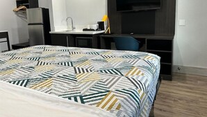 Ein Hotelzimmer mit Bett, Schreibtisch, Stuhl, Fernseher, einer kleinen Küchenzeile und einem Kleiderschrank.