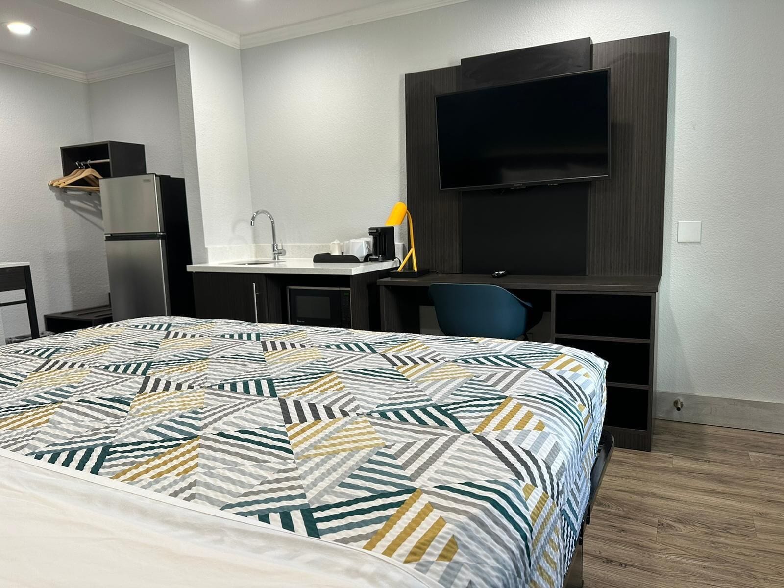 A hotel room with a bed, a desk, a chair, a TV, a microwave, and a wardrobe.