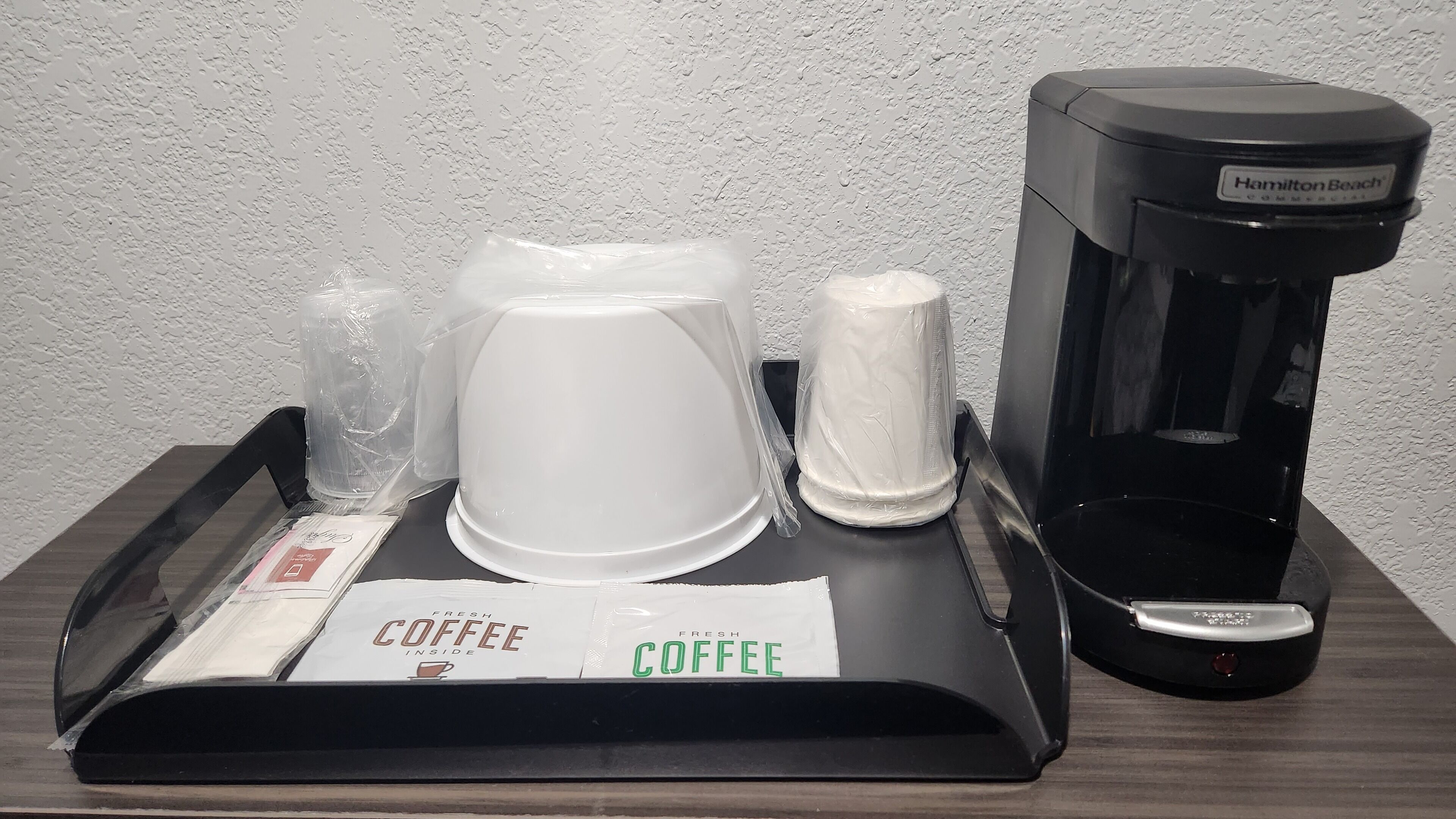 Eine Kaffeemaschine, eine weiße Kaffeekanne und ein Tablett mit einem Kaffeefilter auf einem Holztisch.