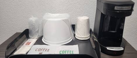 Eine Kaffeemaschine, eine weiße Kaffeekanne und ein Tablett mit einem Kaffeefilter auf einem Holztisch.