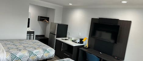 Une chambre d’hôtel de taille réduite comprenant un lit, un bureau avec un lavabo, une chaise, un téléviseur et une armoire.