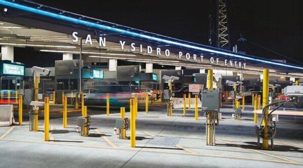 Área de cabina de peaje con múltiples carriles y barreras amarillas, señalada como 'SAN YSIDRO PORT OF ENTRY'.