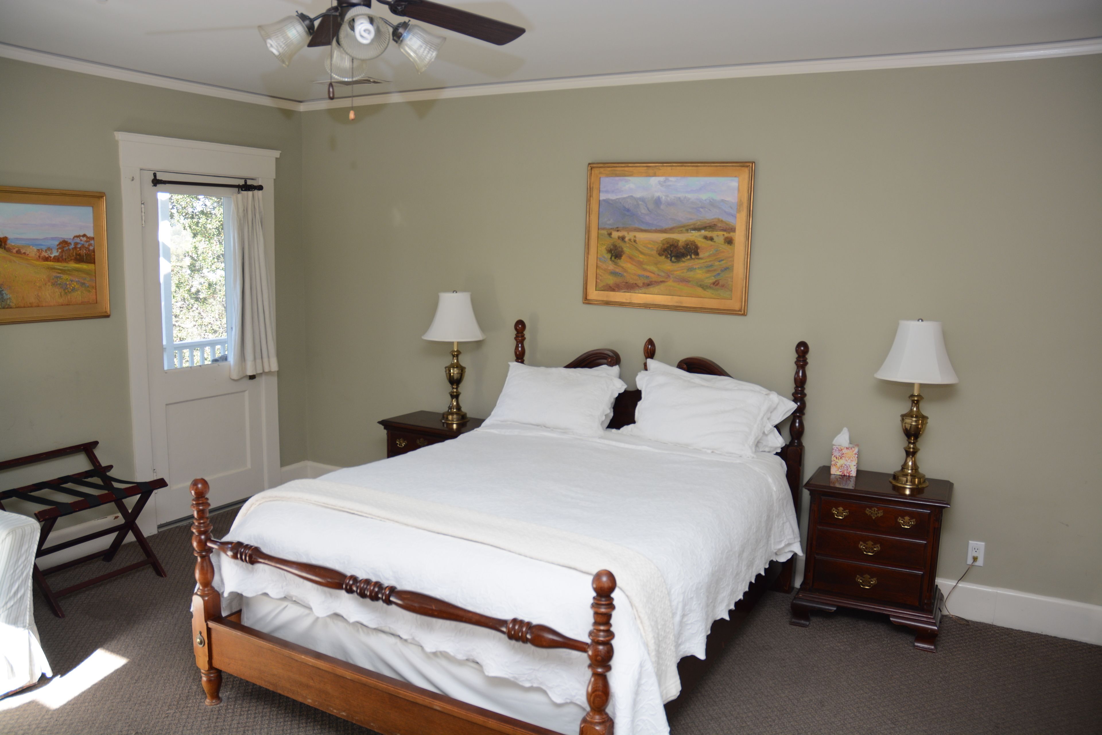 A bedroom with a wooden bed, two bedside tables with lamps, a window with curtains, and a painting on the wall.