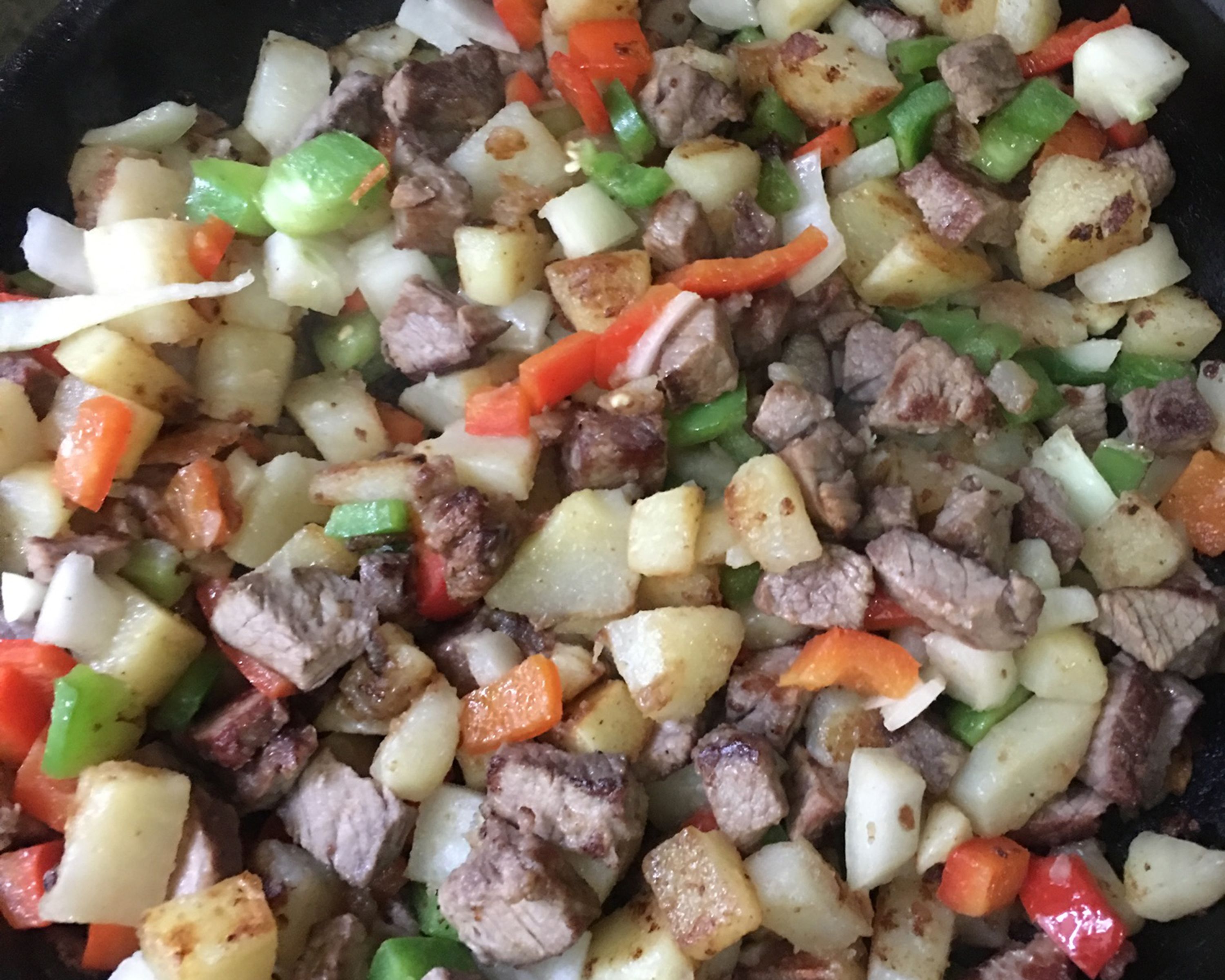 Primer plano de un plato cocinado con papas en cubos, carne y pimientos.