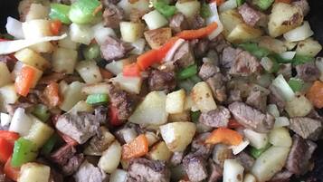 Primer plano de un plato cocinado con papas en cubos, carne y pimientos.