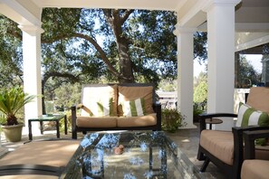 A covered outdoor seating area with a glass table, a sofa with striped cushions, and a potted plant. - Arroyo Vista Inn (South Pasadena)